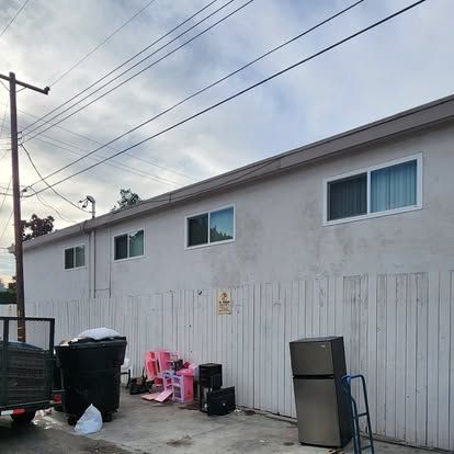 A white building with a fence and a refrigerator in front of it.