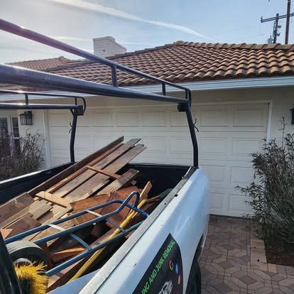 The back of a truck filled with wood is parked in front of a house.