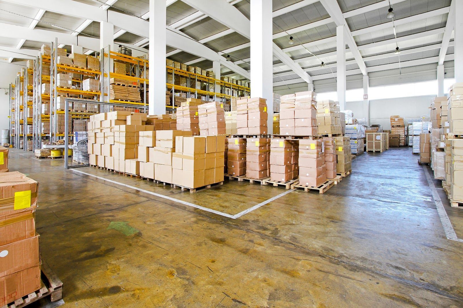 Warehouse interior, stacks of cardboard boxes on pallets and shelves, industrial setting.
