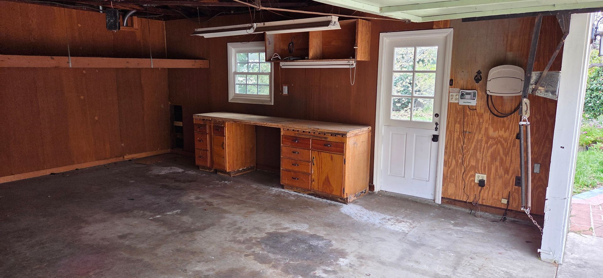 An empty, old garage with wooden walls, workbench, and white door.