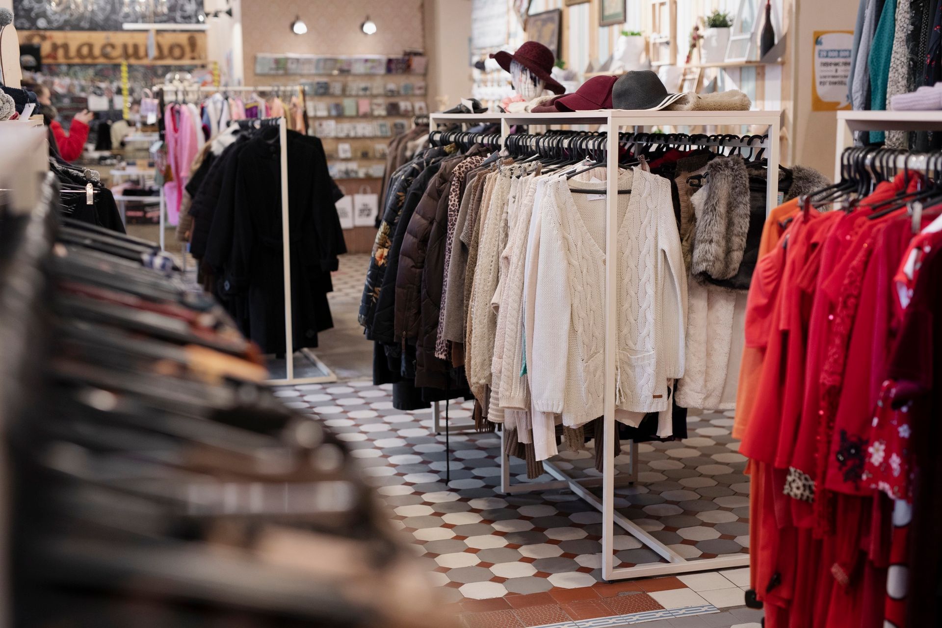 Clothing racks in a boutique, showcasing various garments against a backdrop of shelves and patterned flooring.