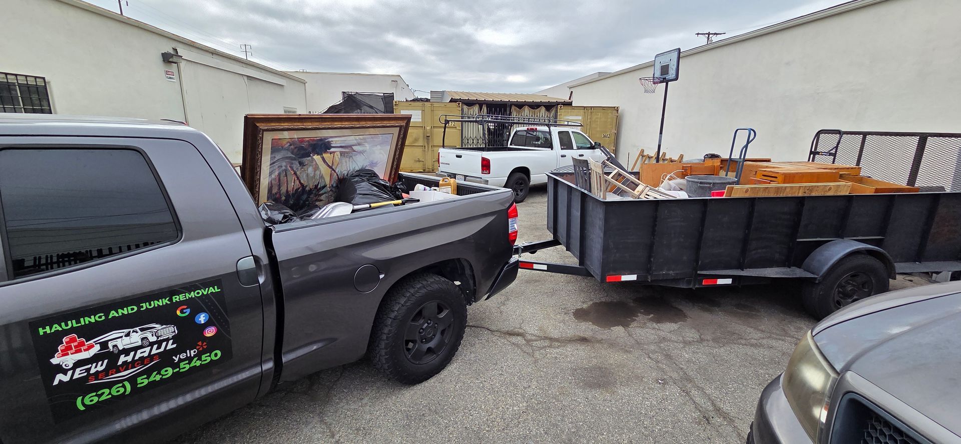 A dark truck and trailer loaded with debris and a frame in an alley.