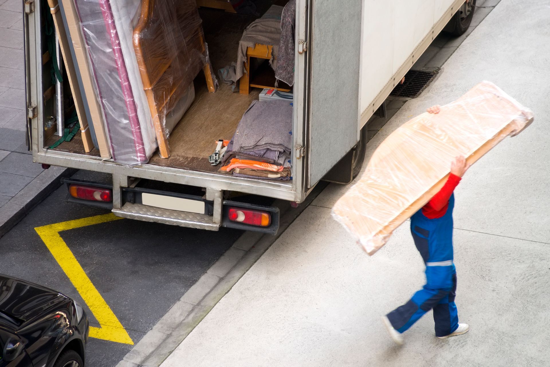 A man is carrying a large piece of wood in front of a moving truck.