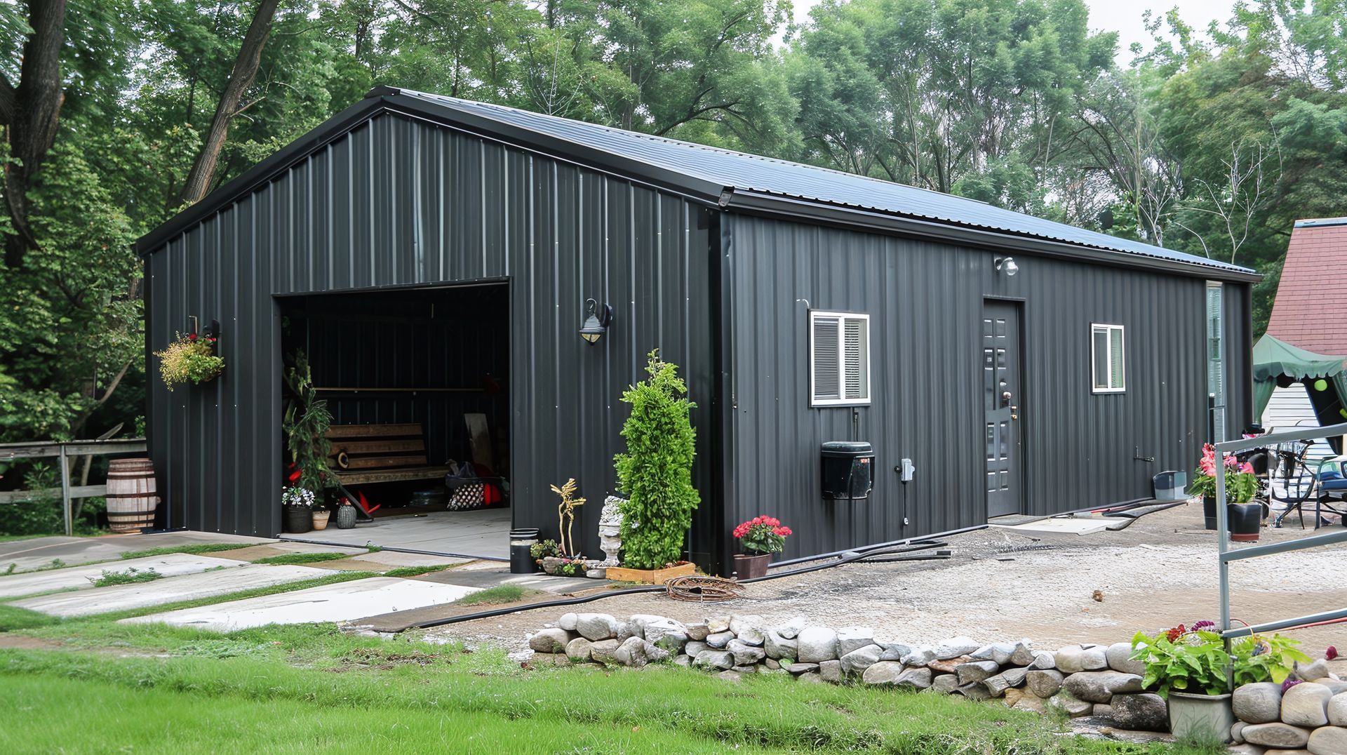 A black garage with a large door is sitting in the middle of a lush green field.