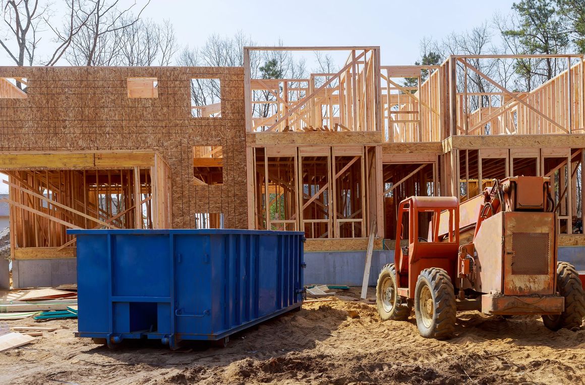 A blue dumpster is sitting in front of a house under construction.