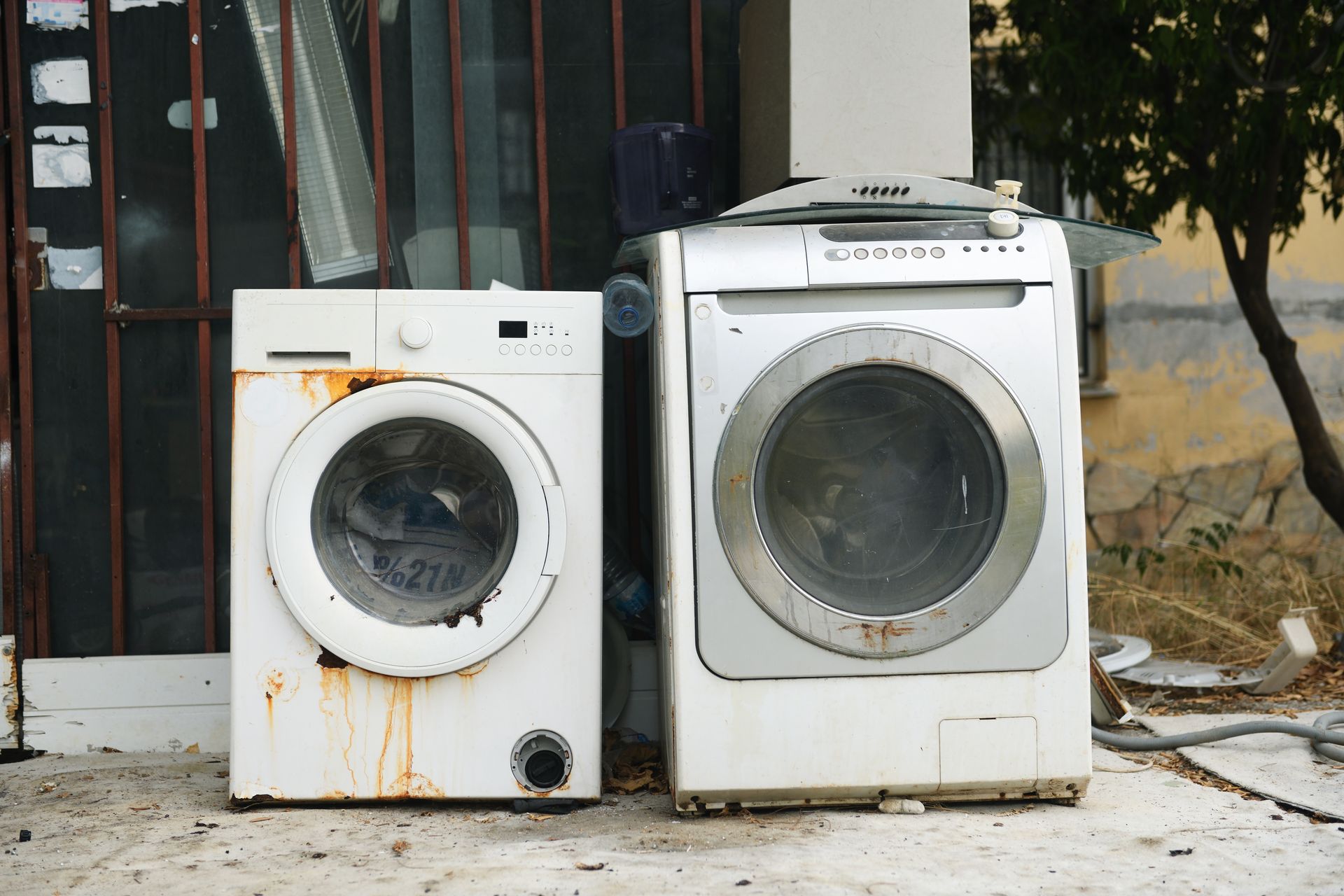 Two old washing machines are sitting next to each other outside of a building.