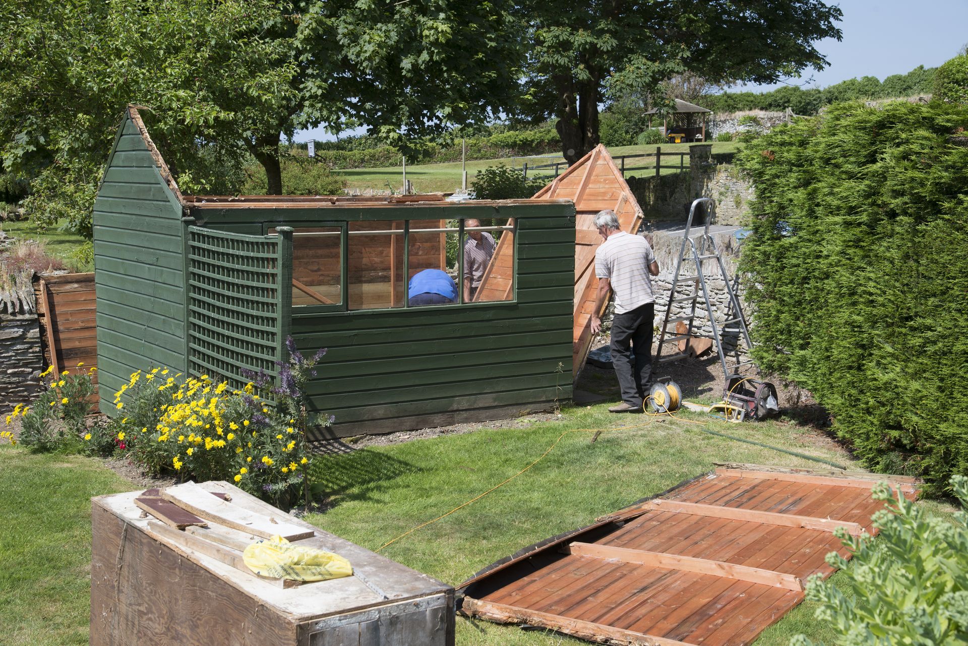 A man is standing in front of a green shed in a garden.