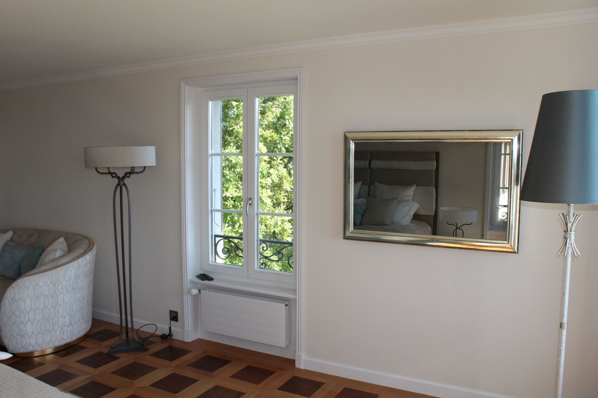 Un salon avec un canapé, une lampe, un miroir et une fenêtre.