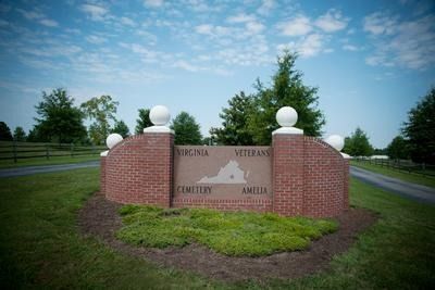 A brick sign with a map of virginia on it is in the middle of a grassy field.