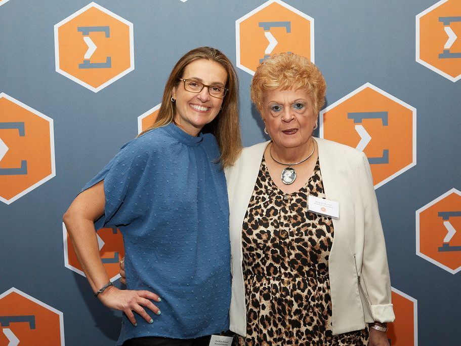 Two women are posing for a picture in front of a wall with the letter f on it