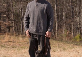 A dog trainer walking a dog on a leash in a field.