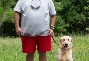 A man is standing next to a dog on a leash in a field.