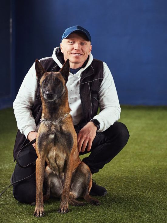 A man is kneeling down next to a dog on the grass.