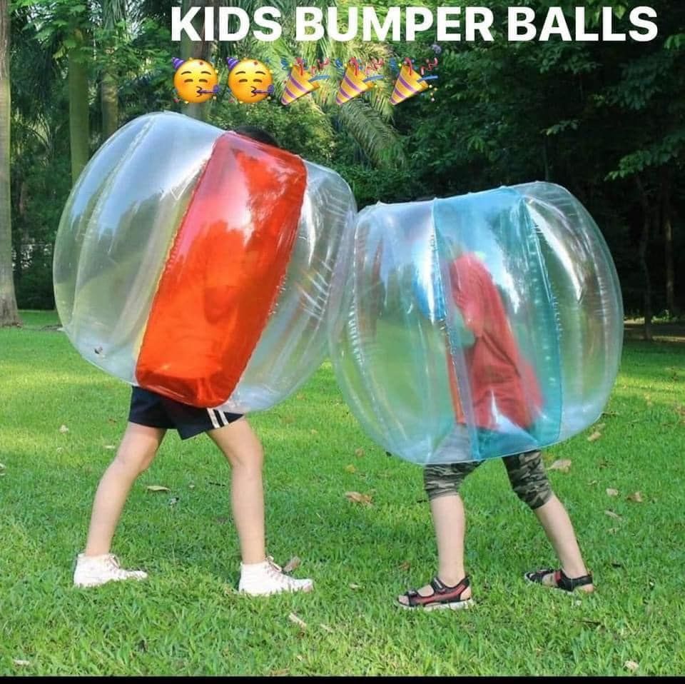 Two kids are playing with bumper balls in the grass