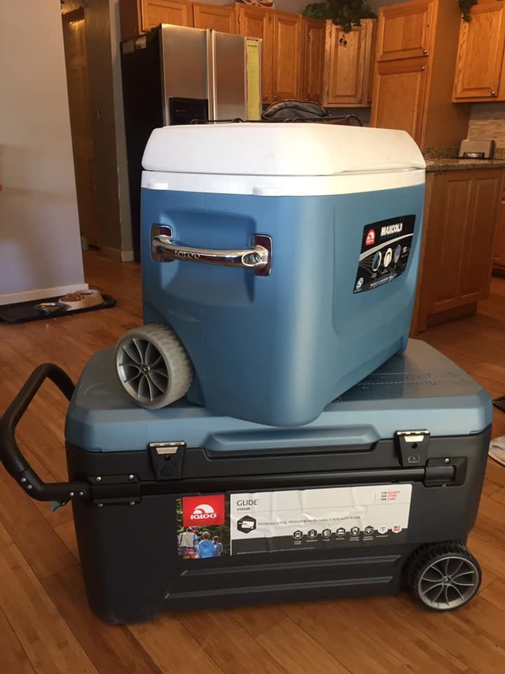 Two coolers with wheels are stacked on top of each other on a wooden floor.