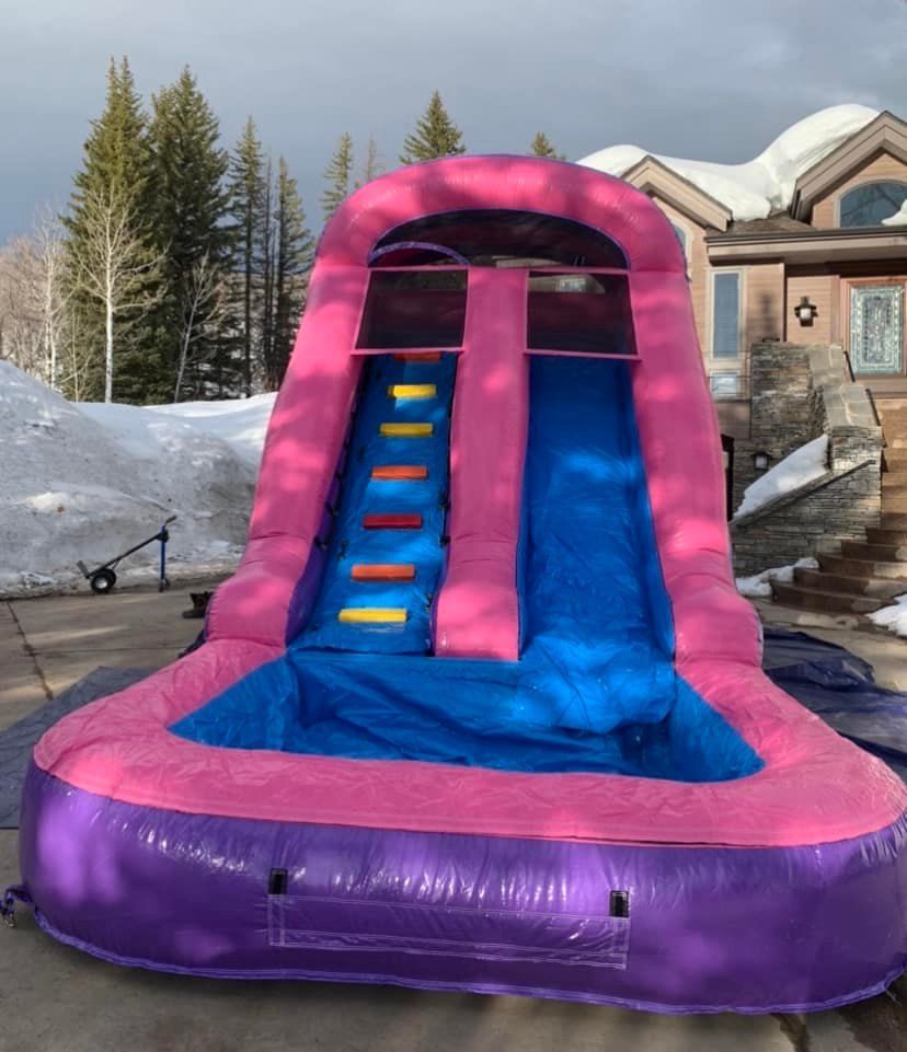 A pink and purple inflatable water slide is sitting in front of a house.