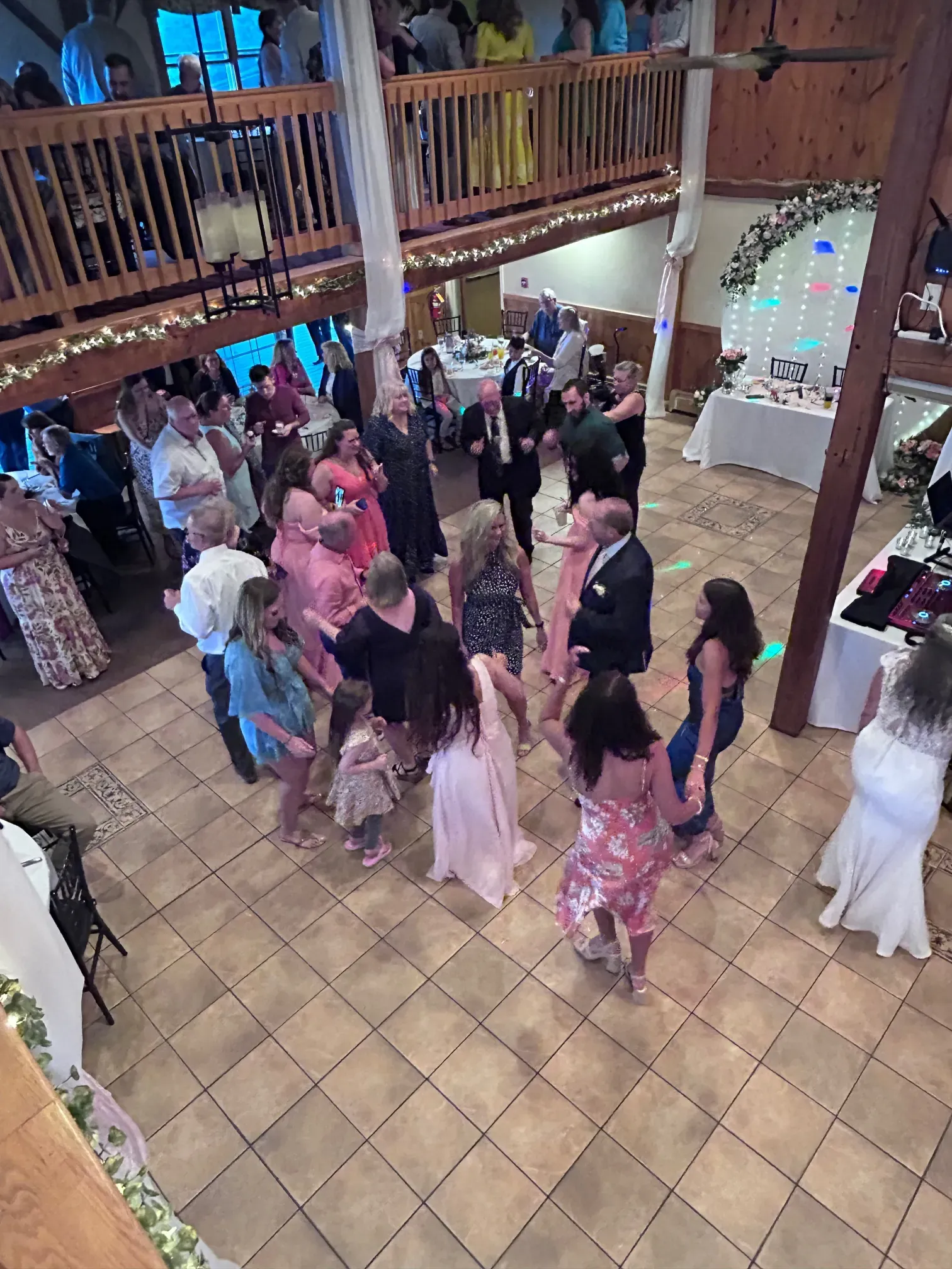 A large group of people are dancing in a large room at a wedding reception.