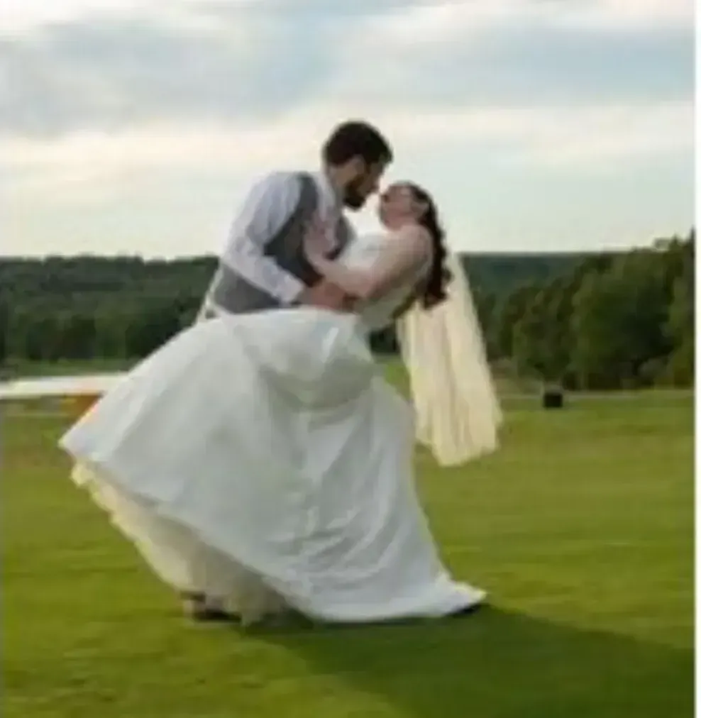 A bride and groom are kissing on a lush green field.