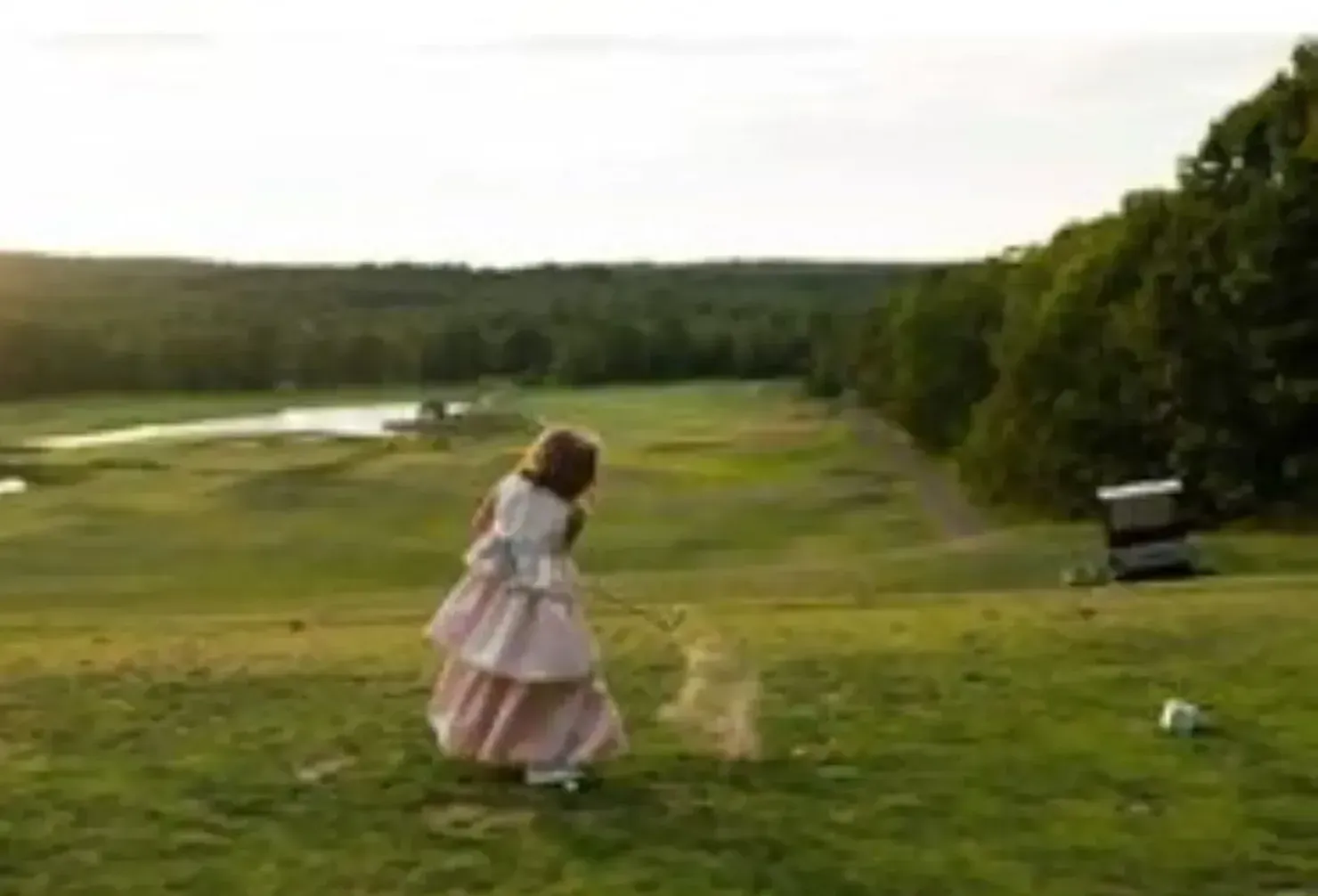 A little girl in a pink dress is standing on a golf course.