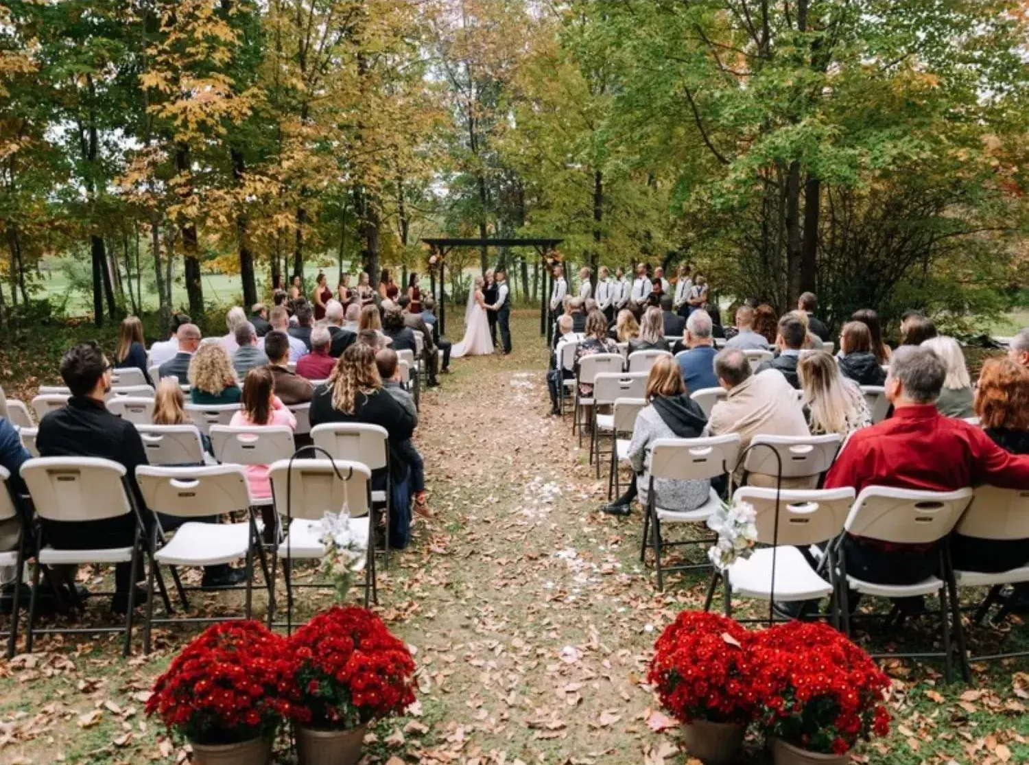 A large group of people are sitting in chairs at a wedding ceremony in the woods.