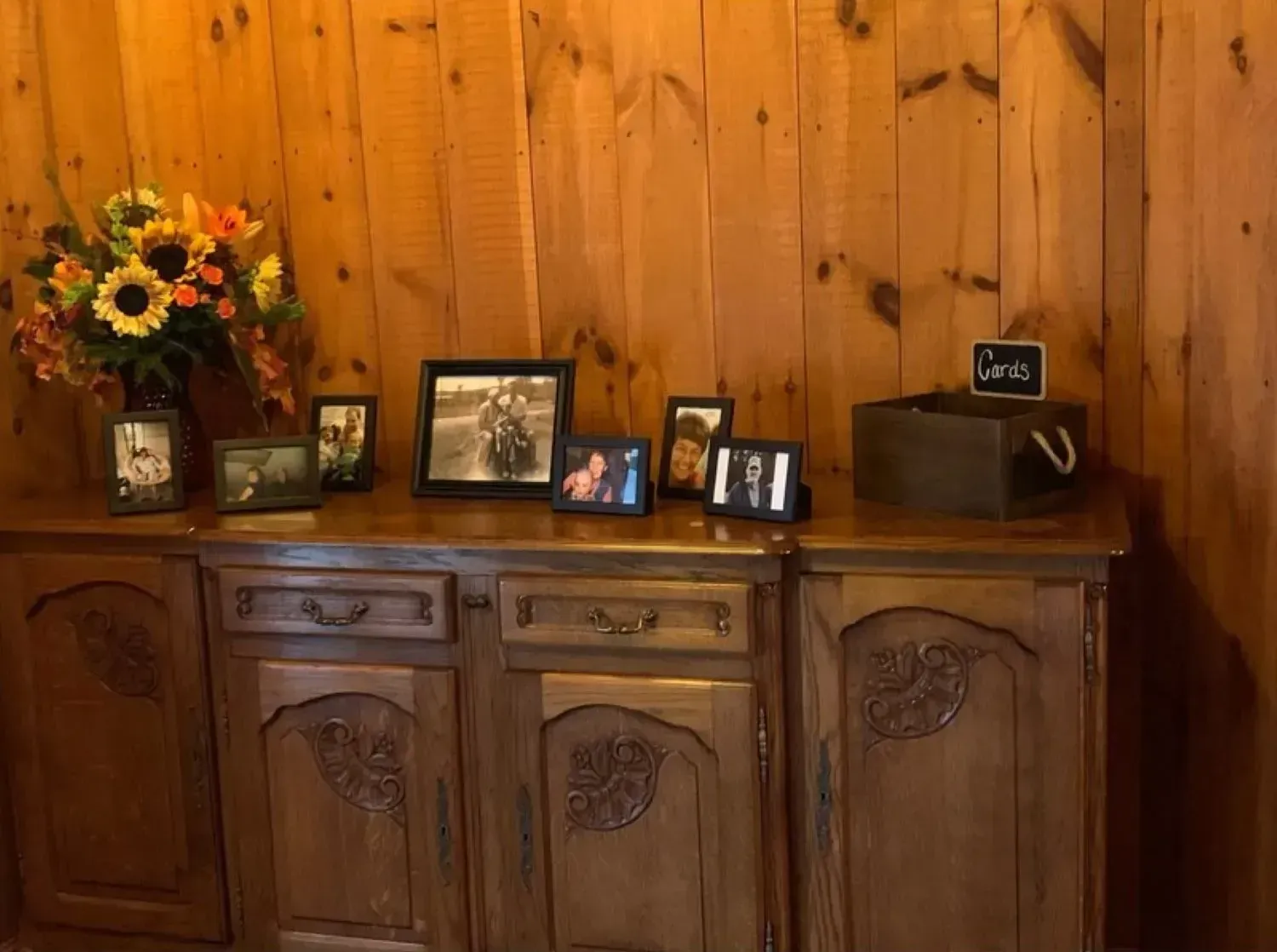 A wooden dresser with pictures on it and a vase of flowers.