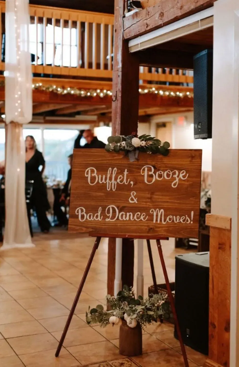 A wooden sign that says `` buffet , booze and bad dance moves '' is on a tripod in a room.