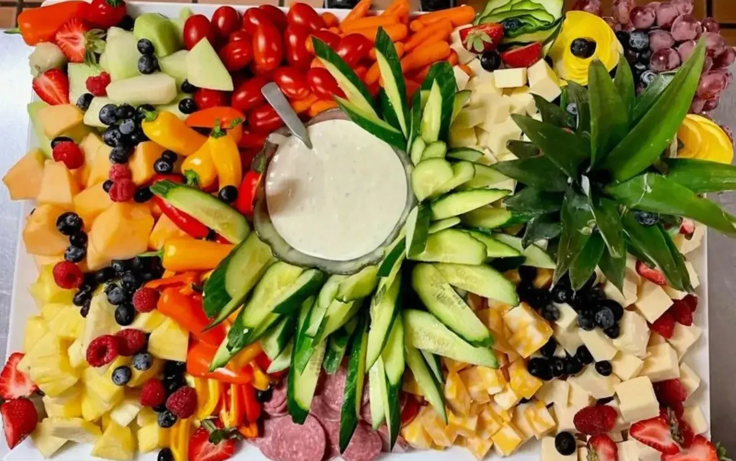 A tray of fruits and vegetables with a dipping sauce on top.