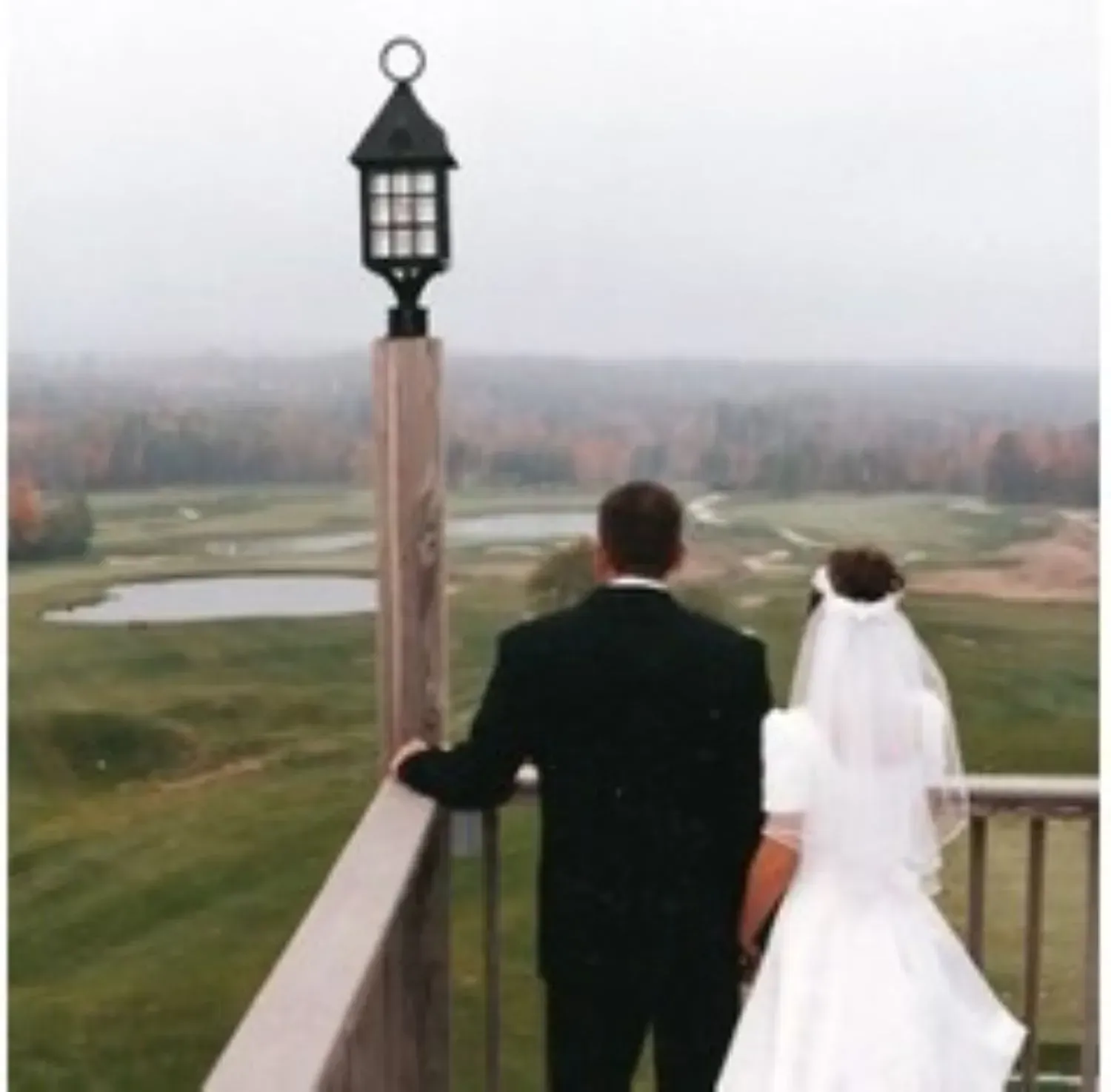 A bride and groom standing on a balcony overlooking a golf course