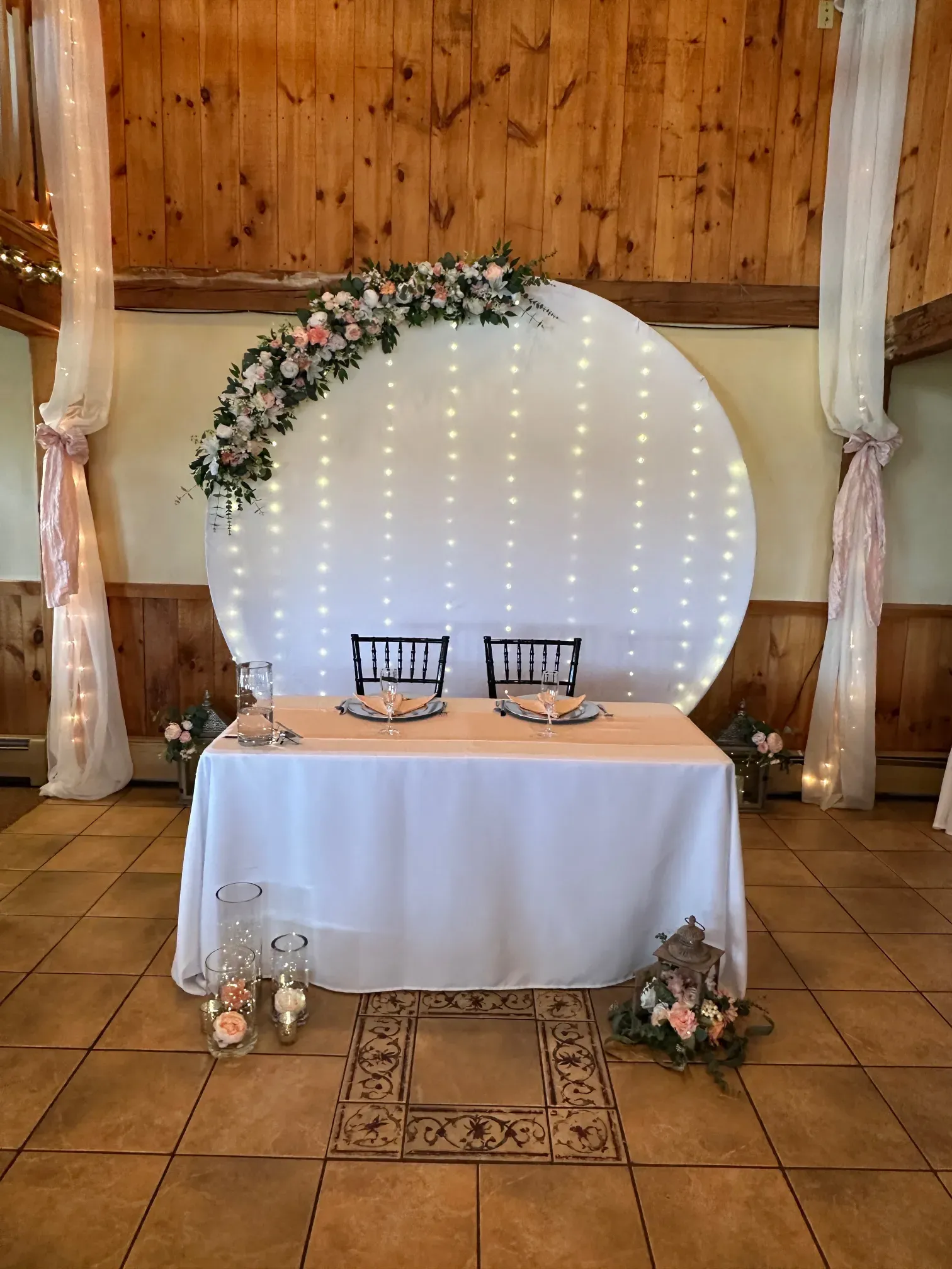 A bride and groom 's table is decorated with flowers and lights for a wedding reception.
