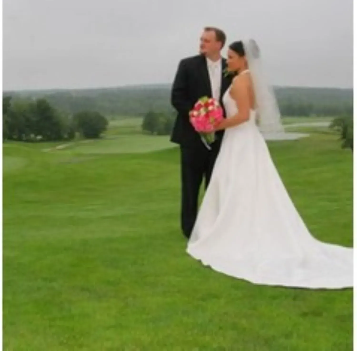 A bride and groom standing on top of a lush green field