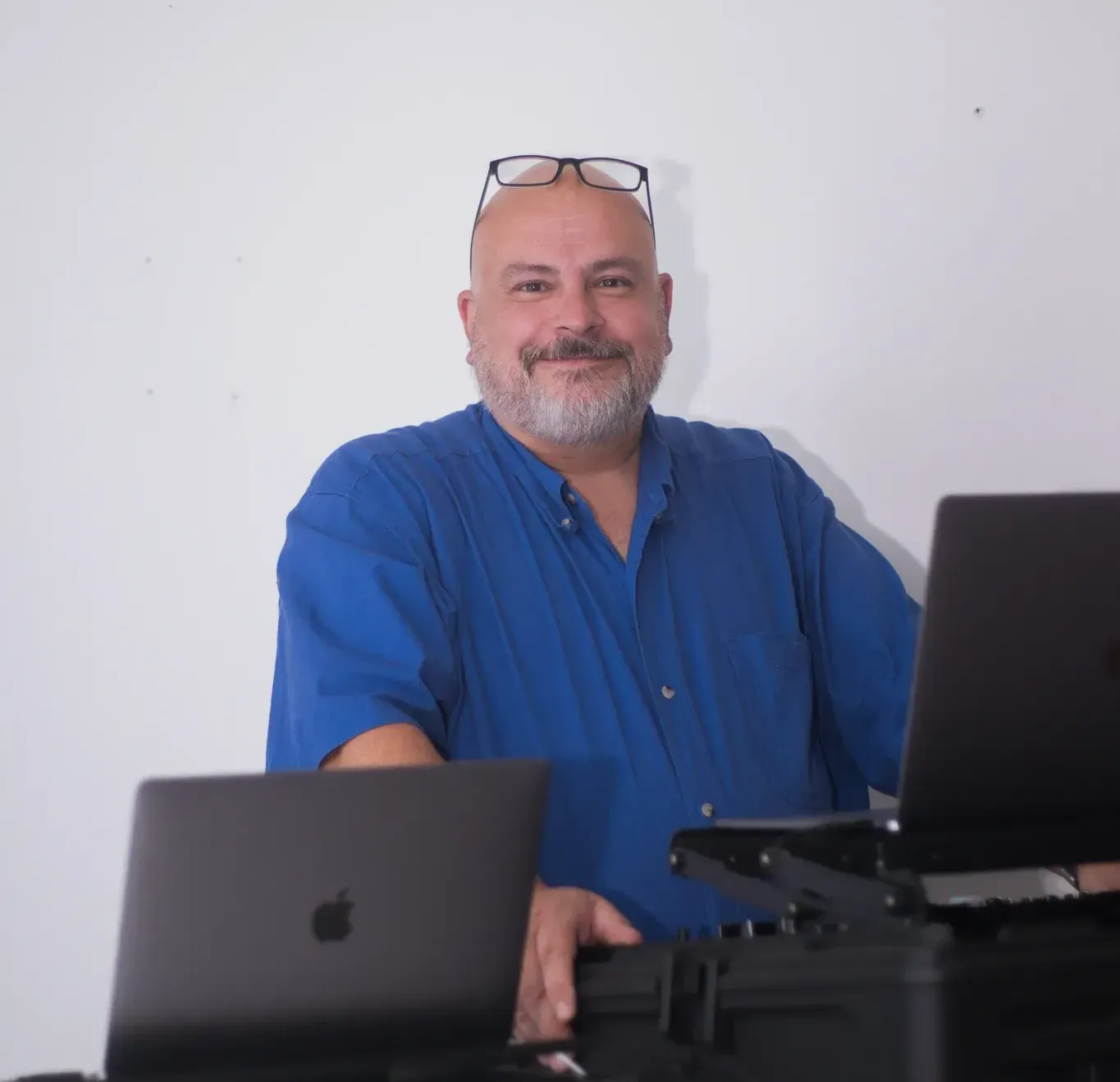 A man in a blue shirt is sitting in front of two apple laptops