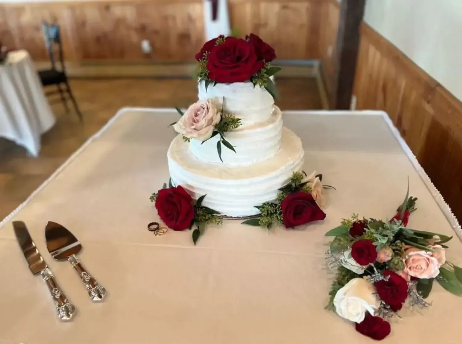 A wedding cake with red roses is sitting on a table.