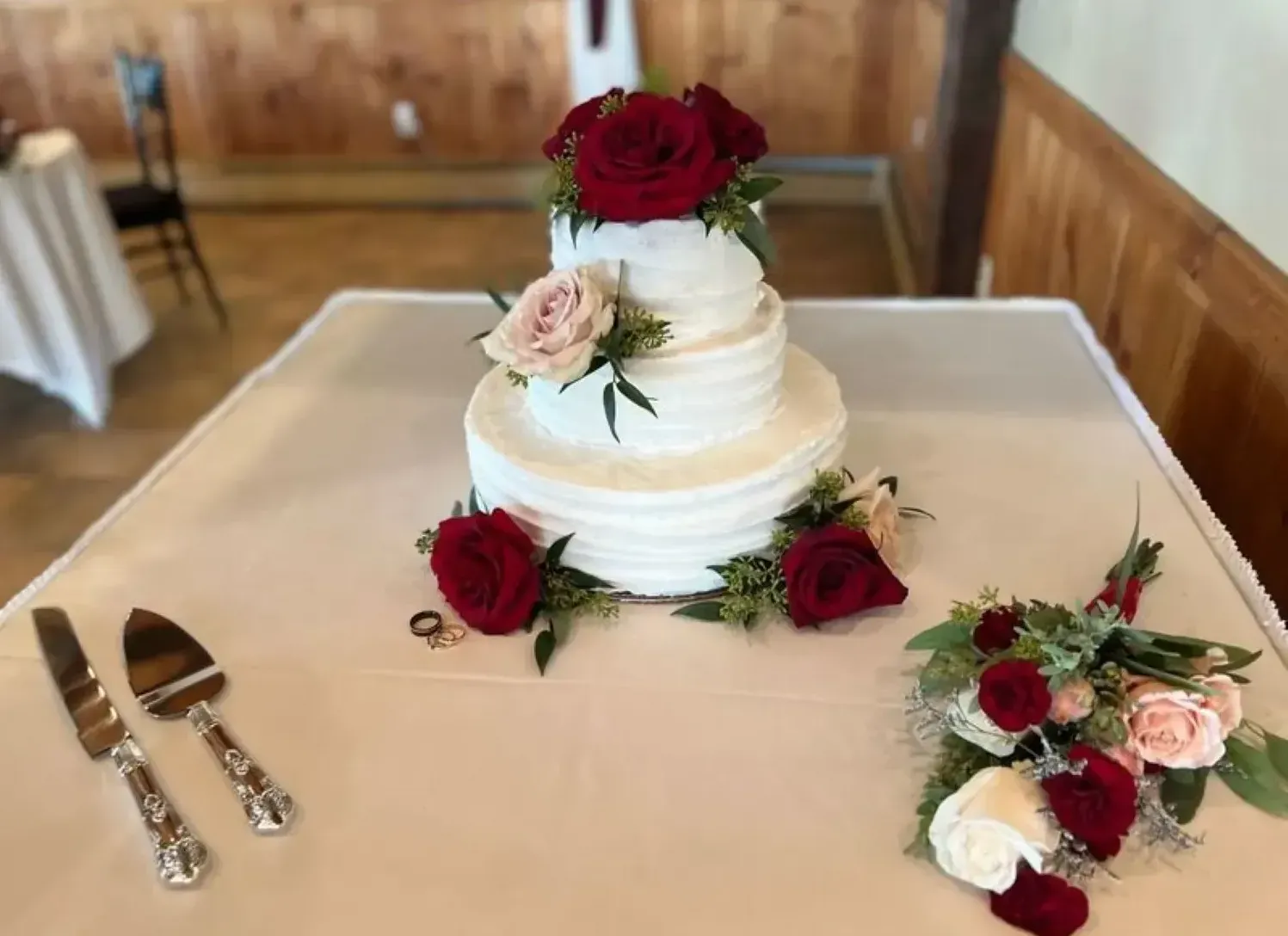 A wedding cake with red roses is sitting on a table.