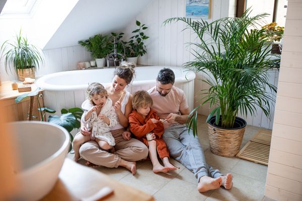 Family of four sitting on the floor, with plants and a bathtub in a bright bathroom.