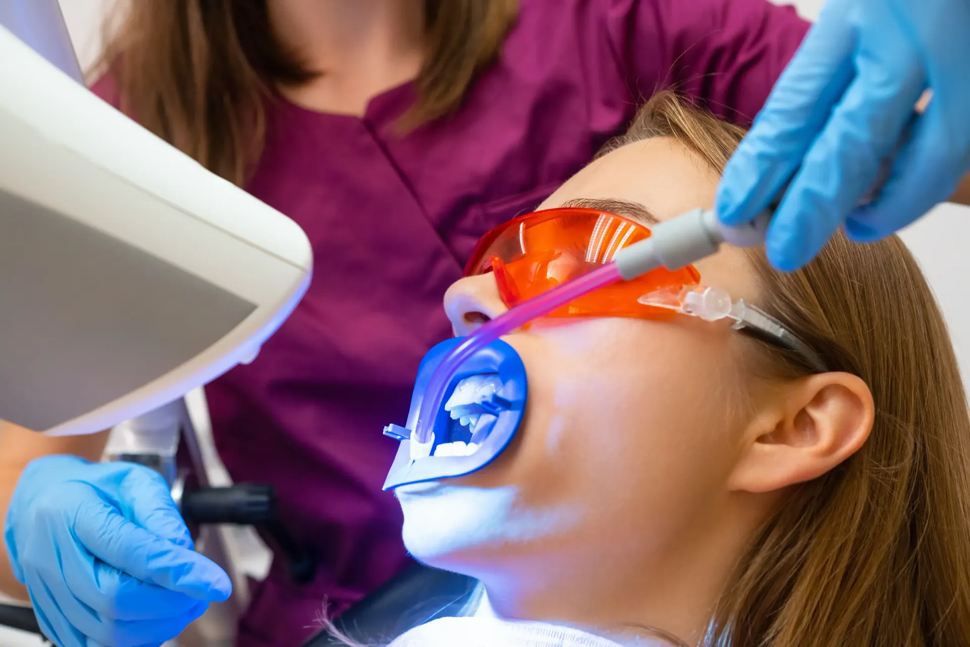 A woman is getting her teeth whitened by a dentist.