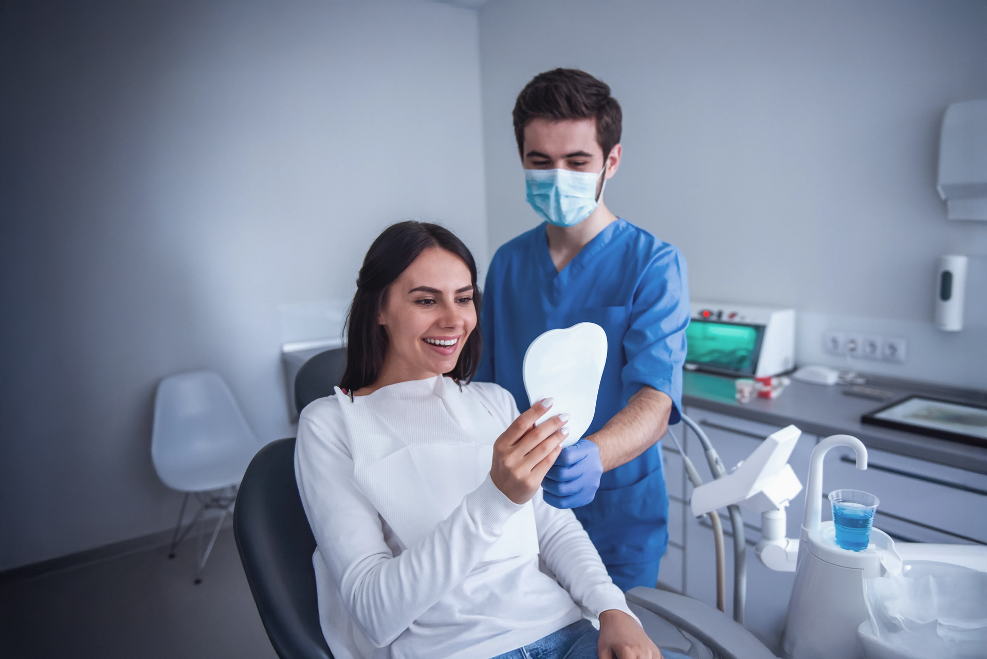A woman is sitting in a dental chair looking at her teeth in a mirror.