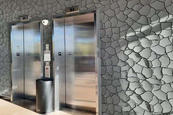Artistic grey wall covering with a textured, cracked design surrounding an elevator at the Dakota Dunes Hotel.