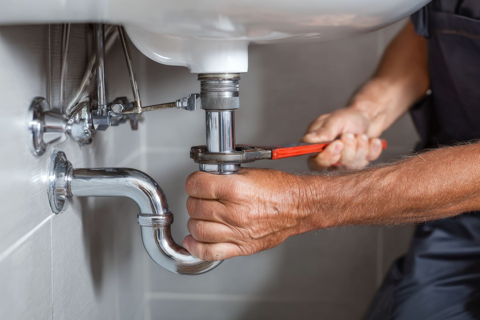 Plumber repairs sink plumbing with a wrench in a modern bathroom.