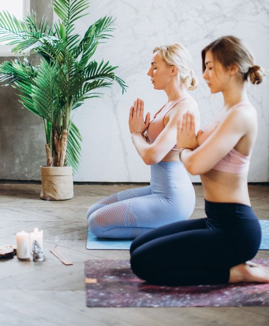 two women sitting with hands in prayer following yoga class