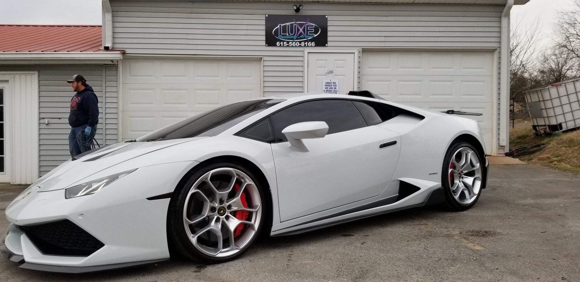 White Lamborghini parked in front of a garage. Man standing next to the car.