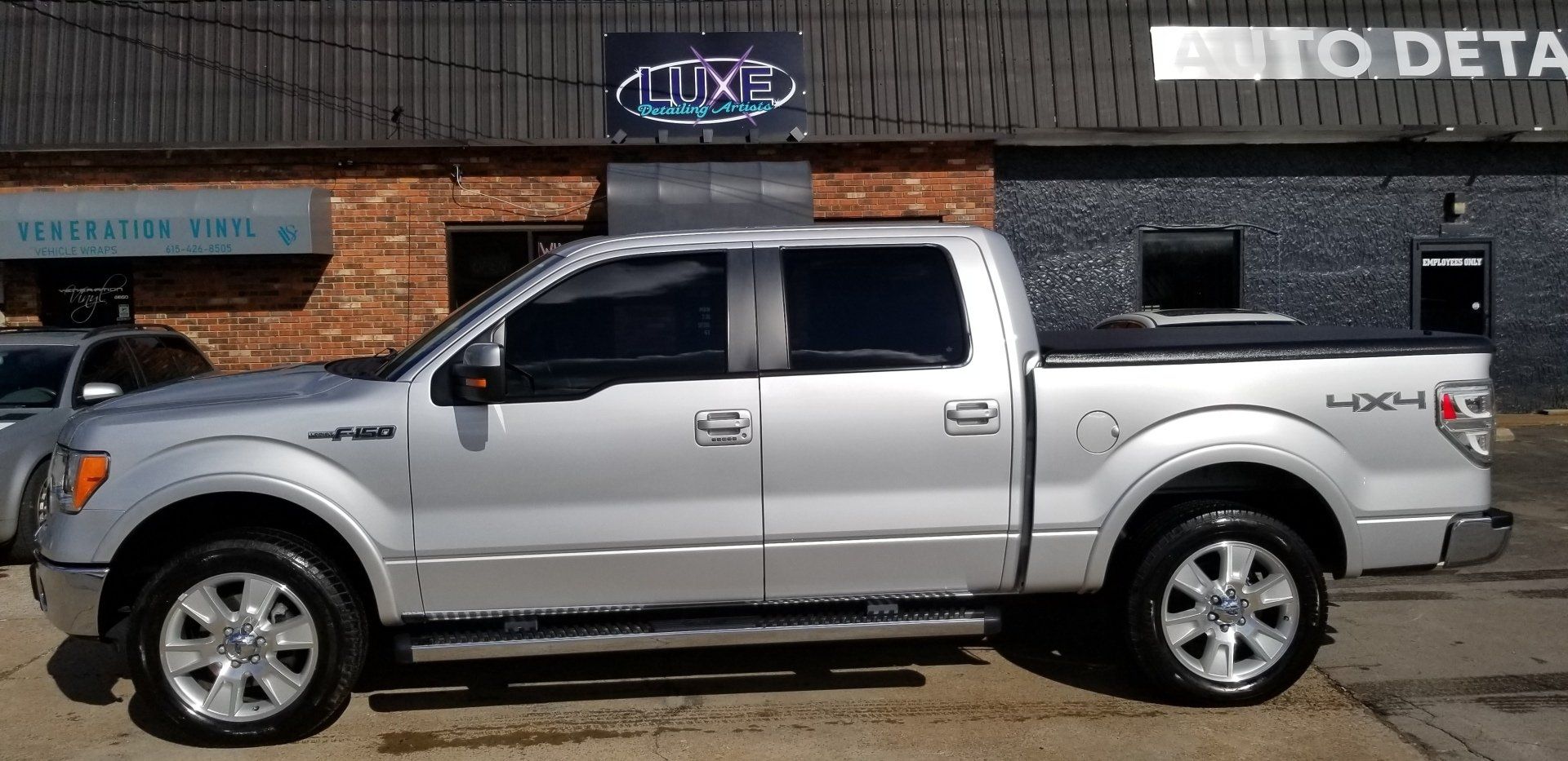 Silver Ford F-150 pickup truck parked outside a brick building, with tinted windows and a black bed cover.