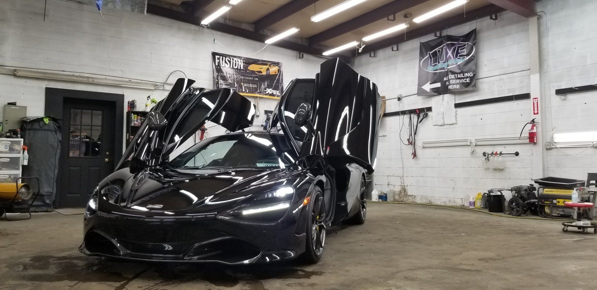 Black McLaren with butterfly doors open inside a garage.