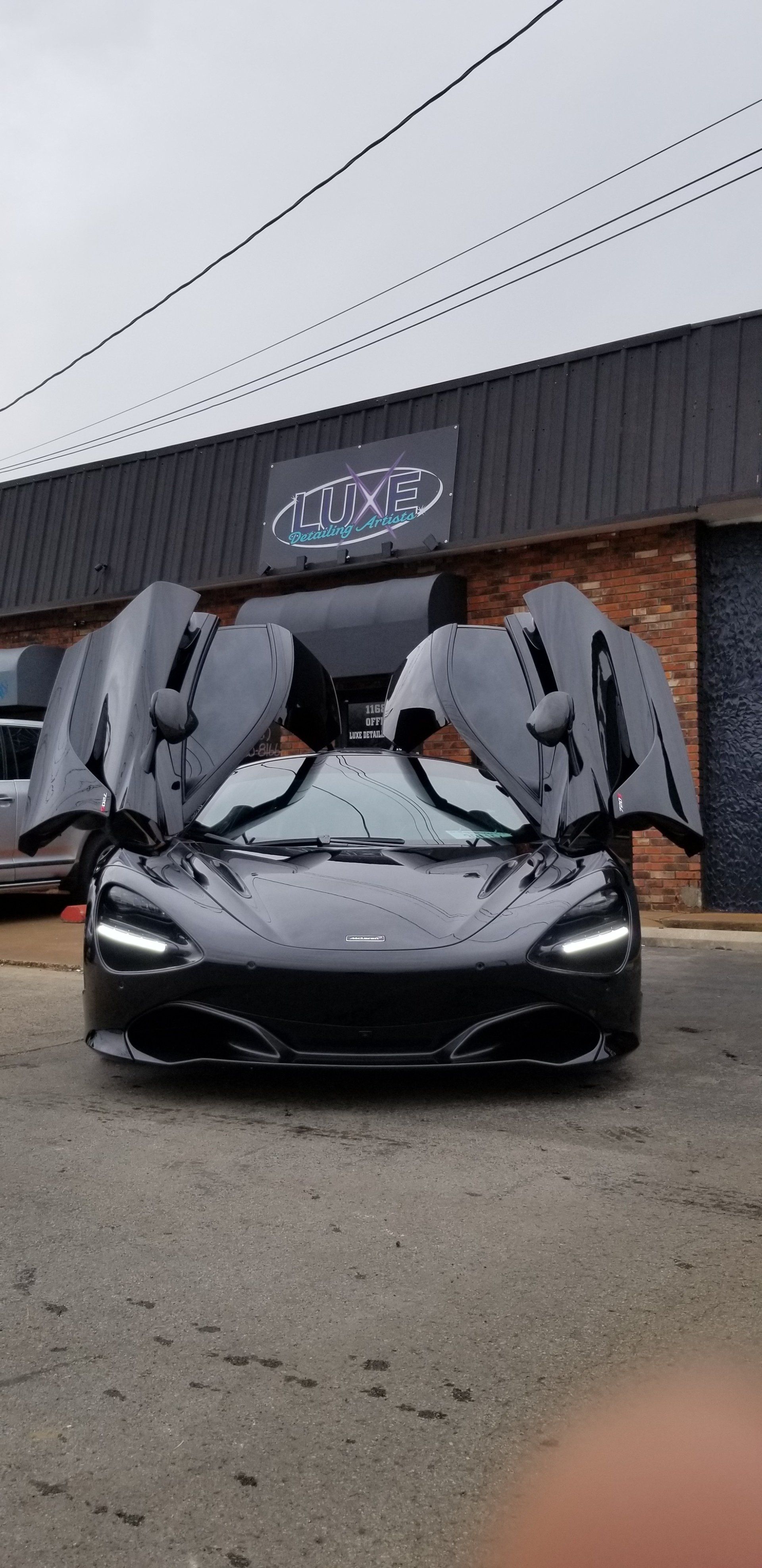 Black McLaren sports car with doors open in front of a business.