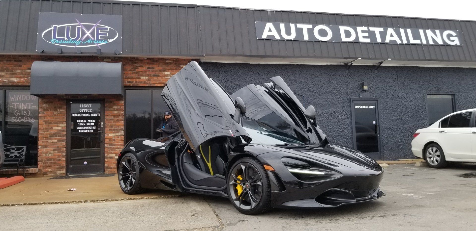 Black McLaren with open doors parked outside an auto detailing shop.