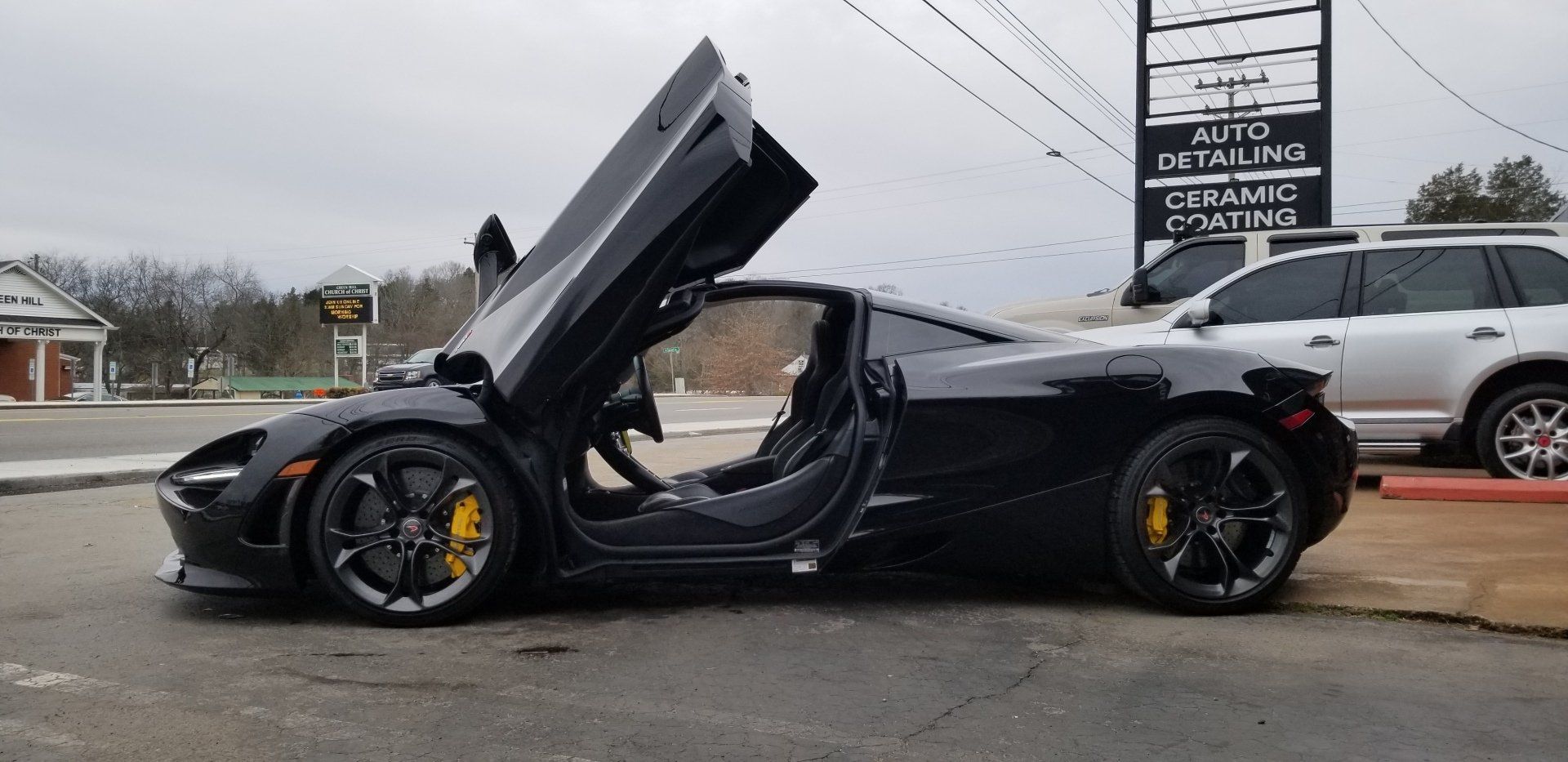Black McLaren sports car with doors open, parked on asphalt, yellow brake calipers.