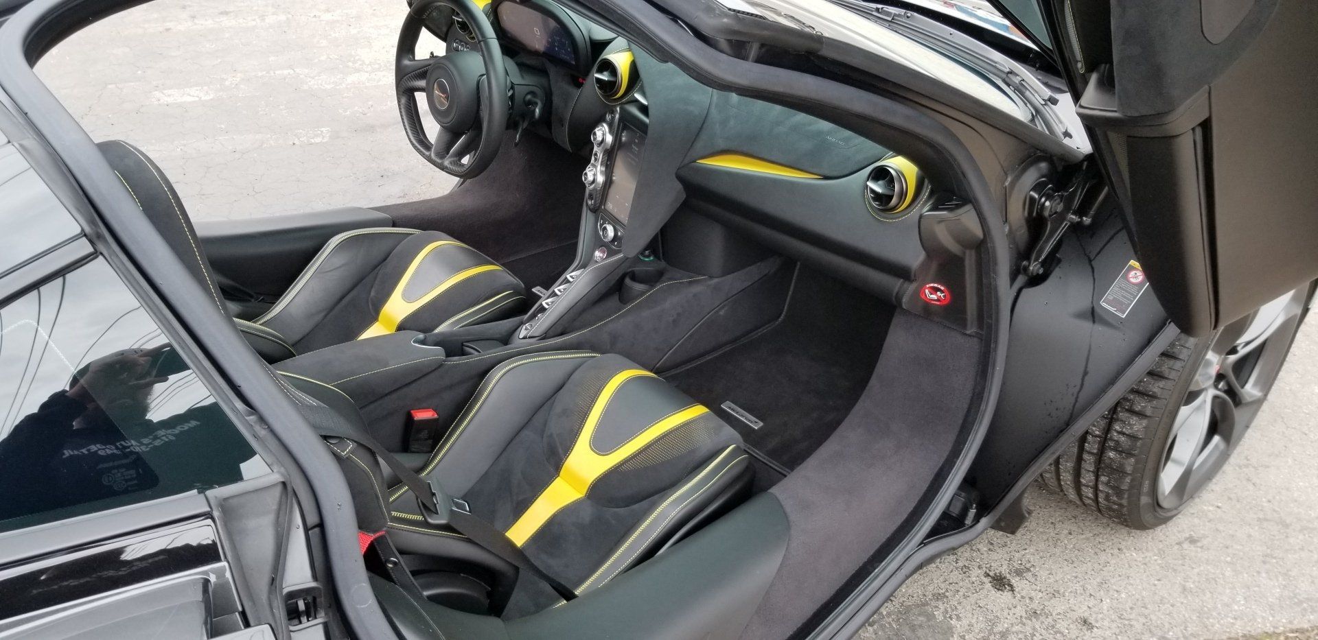 Interior view of a black sports car with yellow accents on the seats and dashboard. Door open.
