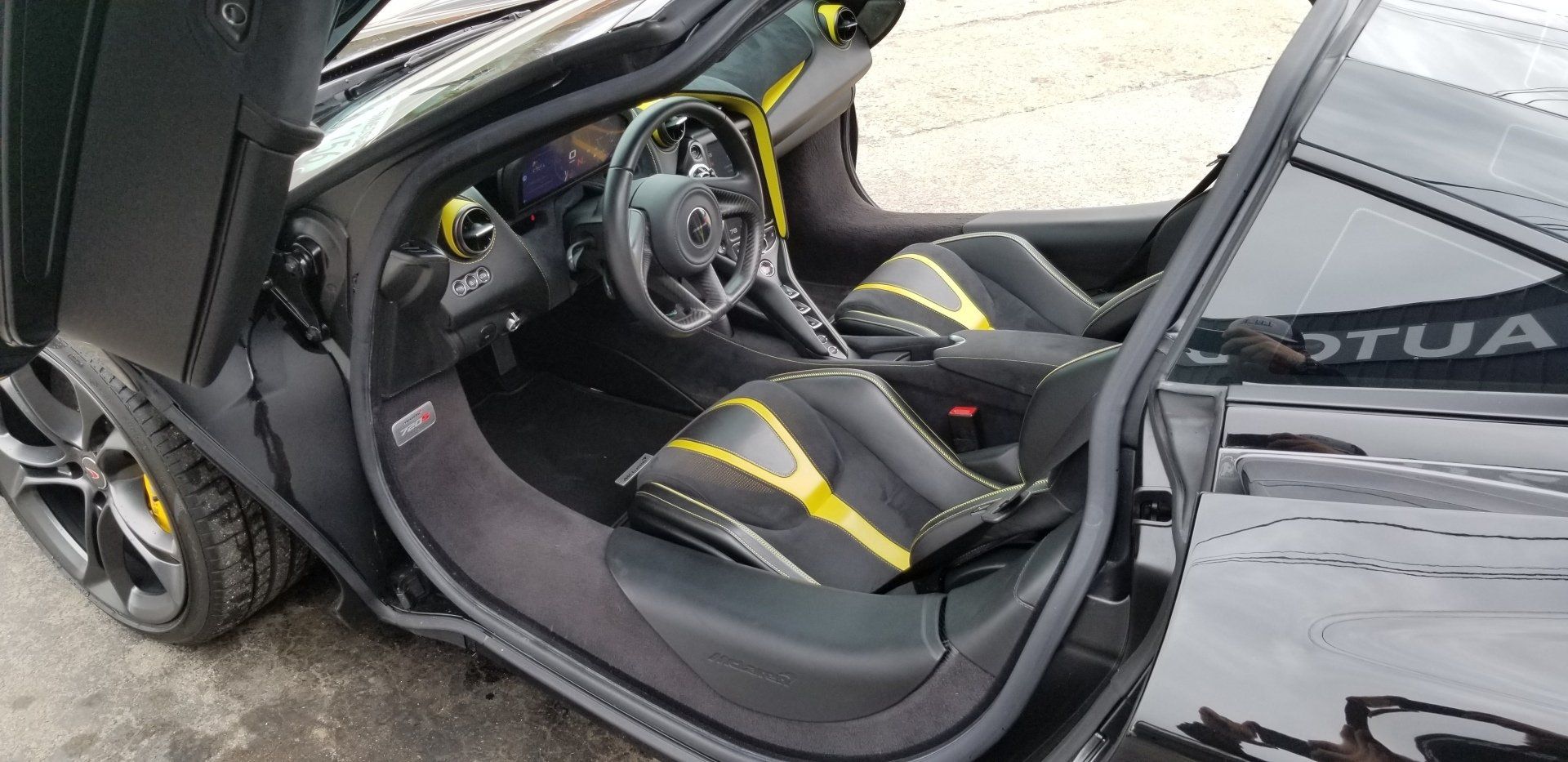 Black McLaren sports car interior, open door. Yellow and black seats.