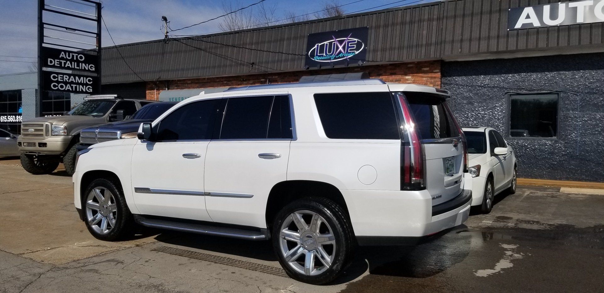 White Cadillac SUV parked outside an auto detailing shop. Other vehicles visible. Sunny day.