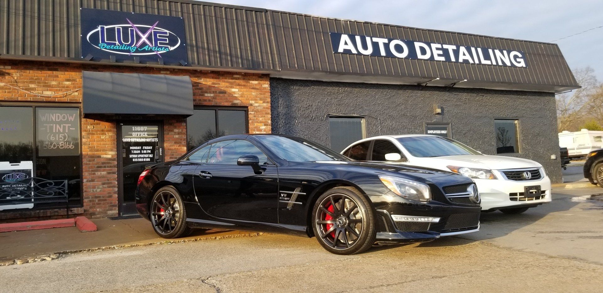 A black car parked outside an auto detailing shop, with a white car next to it.