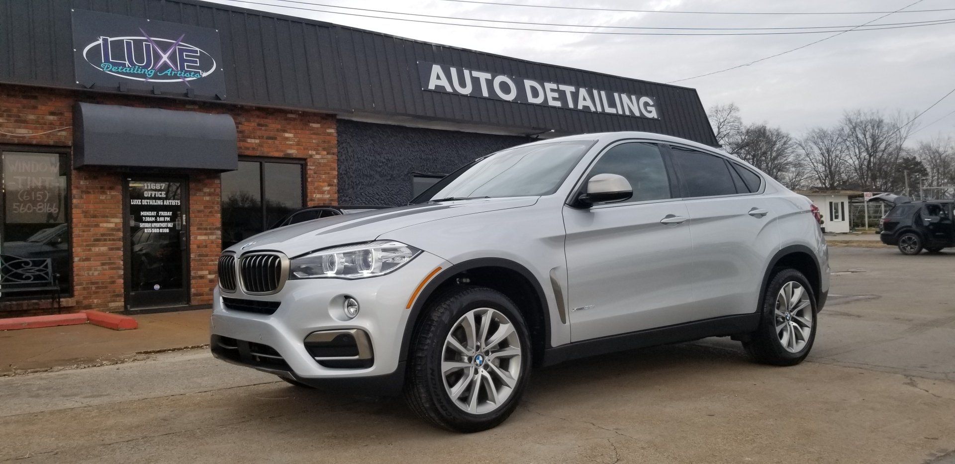 Silver BMW SUV parked outside an auto detailing shop.